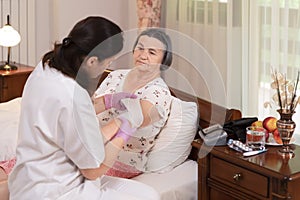 Female doctor bandages senior woman elbow at home