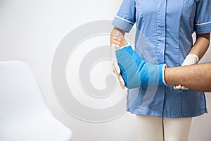 Female doctor in a blue medical gown checking broken leg on male patient