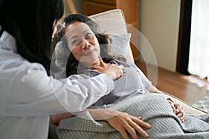 Female doctor cardiologist checking up her elderly patient`s listening heartbeat by stethoscope