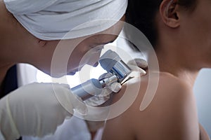 Female doctor checking woman body with dermatoscopy