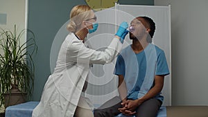 Female doctor checking young adult man for sore throat indoors