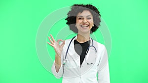 Female doctor, close-up, on a green background, shows the ok sign