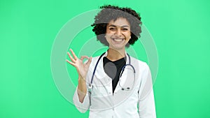 Female doctor, close-up, on a green background, shows the ok sign