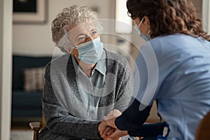 Female doctor consoling senior woman wearing face mask during home visit