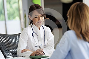 Female doctor consulting her patient while sitting at desk in doctor`s office photo