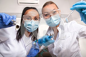 Female doctor dentist and assistant in masks looking at camera