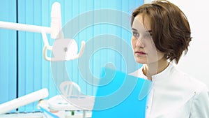 Female doctor in dentist cabinet reading patient notes in front of medical equipment, healthcare concept. Female dentist