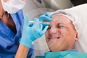 Female doctor is doing injection to patient in skin of face