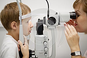 Female doctor examines eyes of boy through slit photo