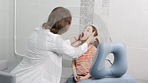 a female doctor examines the neck and mouth of a little girl in the clinic.