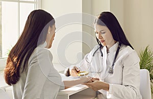 Female doctor examining hand skin of a young woman patient using magnifying glass.