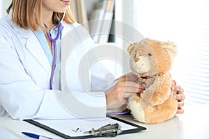 Female doctor examining a nTeddy bear patient by stethoscope. photo