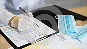 Female doctor filling medical form on clipboard holding ballpoint.