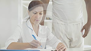 Female doctor filling in medical forms and talking to patient explaining informed consent to experimental treatment