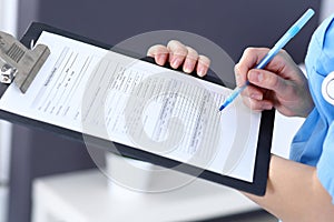 Female doctor filling up medical form on clipboard, closeup. Physician finishing up examining his patient in hospita