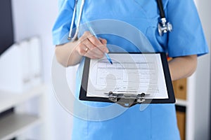 Female doctor filling up medical form on clipboard, closeup. Physician finishing up examining his patient in hospita