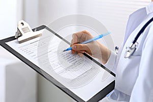 Female doctor filling up medical form on clipboard closeup. Physician finishing up examining his patient in hospital an