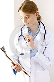 Female doctor filling up medical form on clipboard closeup. Physician finishing up examining his patient in hospital an