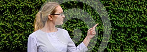 Female doctor with finger point up. Nutritionist in white coat and glasses on green foliage background with copy space. Image for