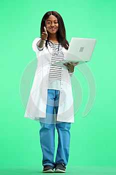 A female doctor, full-length, on a green background, uses a laptop