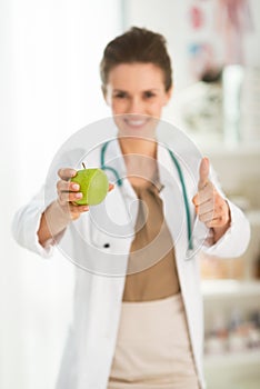 Female doctorÃÂ giving green apple and showing thumbs up. Closeup photo