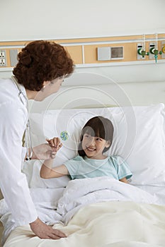 Female doctor giving a lollipop to a young girl lying in a hospital bed