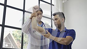 Female doctor giving male patient physiotherapy with hand lift, Asian female physiotherapist working