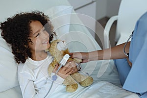 Female doctor giving teddy bear to child patient in the ward