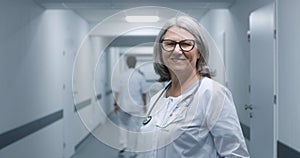 Female doctor in glasses stands in clinic corridor, looks at camera