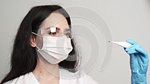 Female doctor in gloves holding an electronic thermometer.