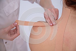 Female doctor glues kinesio tapes on the patient& x27;s shoulder.