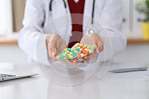 Female doctor hand holding pack of different tablet blisters at workplace closeup