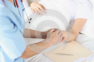 Female doctor hand holds hands of lying patient in hospital