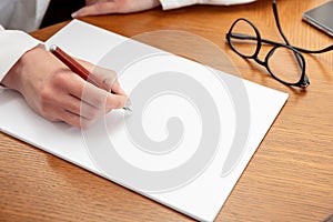 Female doctor hand with a pen on a blank paper, close up, wooden office table, close up above view