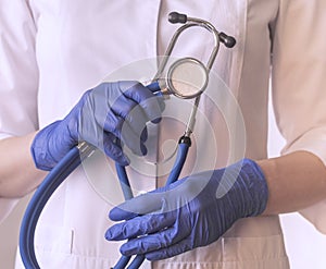 Female doctor hands closeup, holding metal modern stethoscope in hands. Physician with hospital tool and blue latex