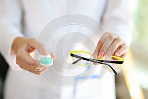Female doctor hands holding pair of glasses and contact lens