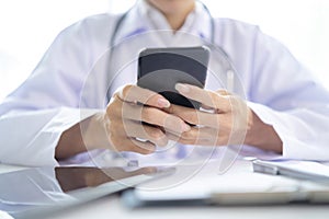 Female doctor hands holding and using mobile smart phone with laptop computer and stethoscope on the table