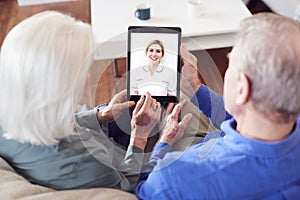 Female Doctor Having Video Consultation With Senior Couple On Digital Tablet At Home