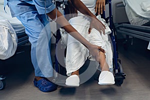 Female doctor helping disabled female patient to move her legs in the ward at hospital