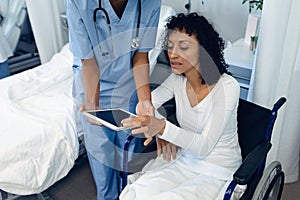 Female doctor helping disabled female patient to use digital tablet in the ward