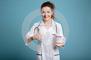 Female doctor holding bottle of pills and showing thumb up