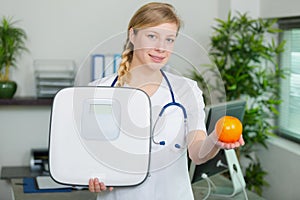 female doctor holding fruit and bathroom scales
