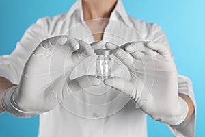 Female doctor holding glass vial on color background, closeup.