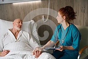 Female doctor holding hand of elderly male patient on bed at the hospital