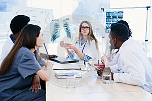 Female doctor holding in hands x ray result on the meeting at modern clinic.. Professional doctors of multi ethnic group