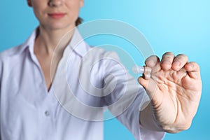 Female doctor holding hearing aid on color background