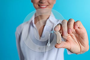 Female doctor holding hearing aid on color background, closeup.