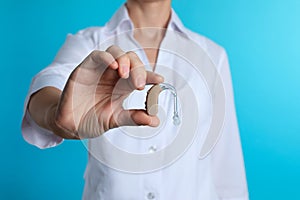 Female doctor holding hearing aid on color background, closeup.