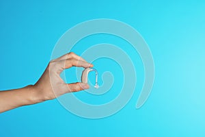 Female doctor holding hearing aid on color background, closeup view with space for text.