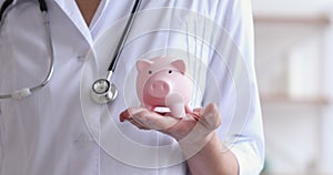 Female doctor holding piggy bank box in hands, closeup view